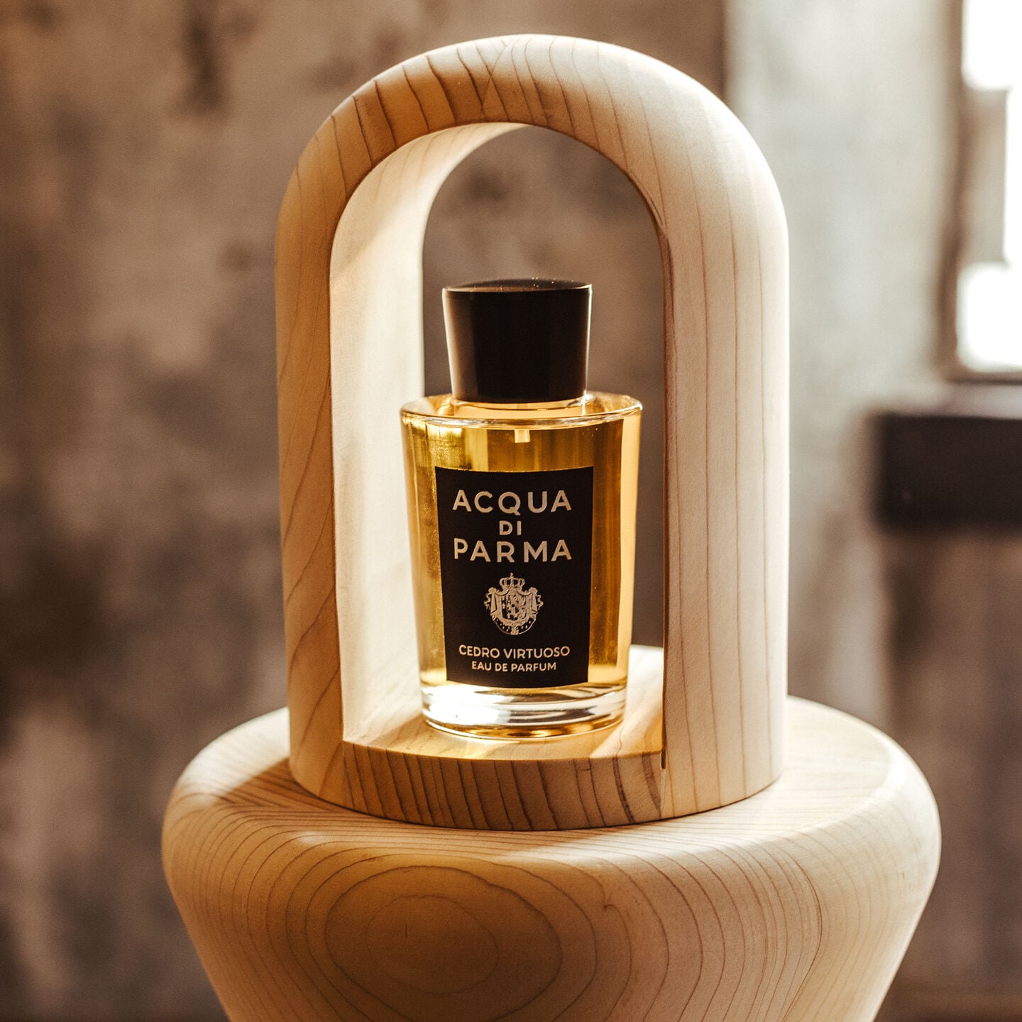 A bottle of Acqua di Parma Cedro Virtuoso framed by a sculptural arch of pale wood in warm sunlight.