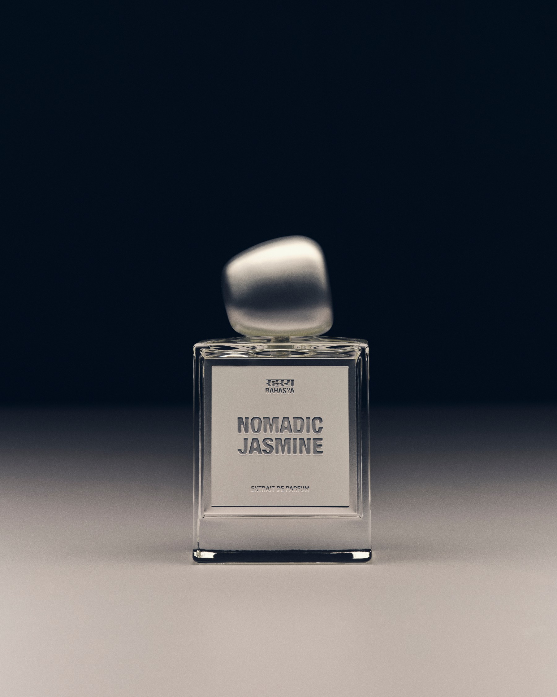 A clear bottle of Rahasya Nomadic Jasmine with a silver label and frosted cap in dark, soft light.